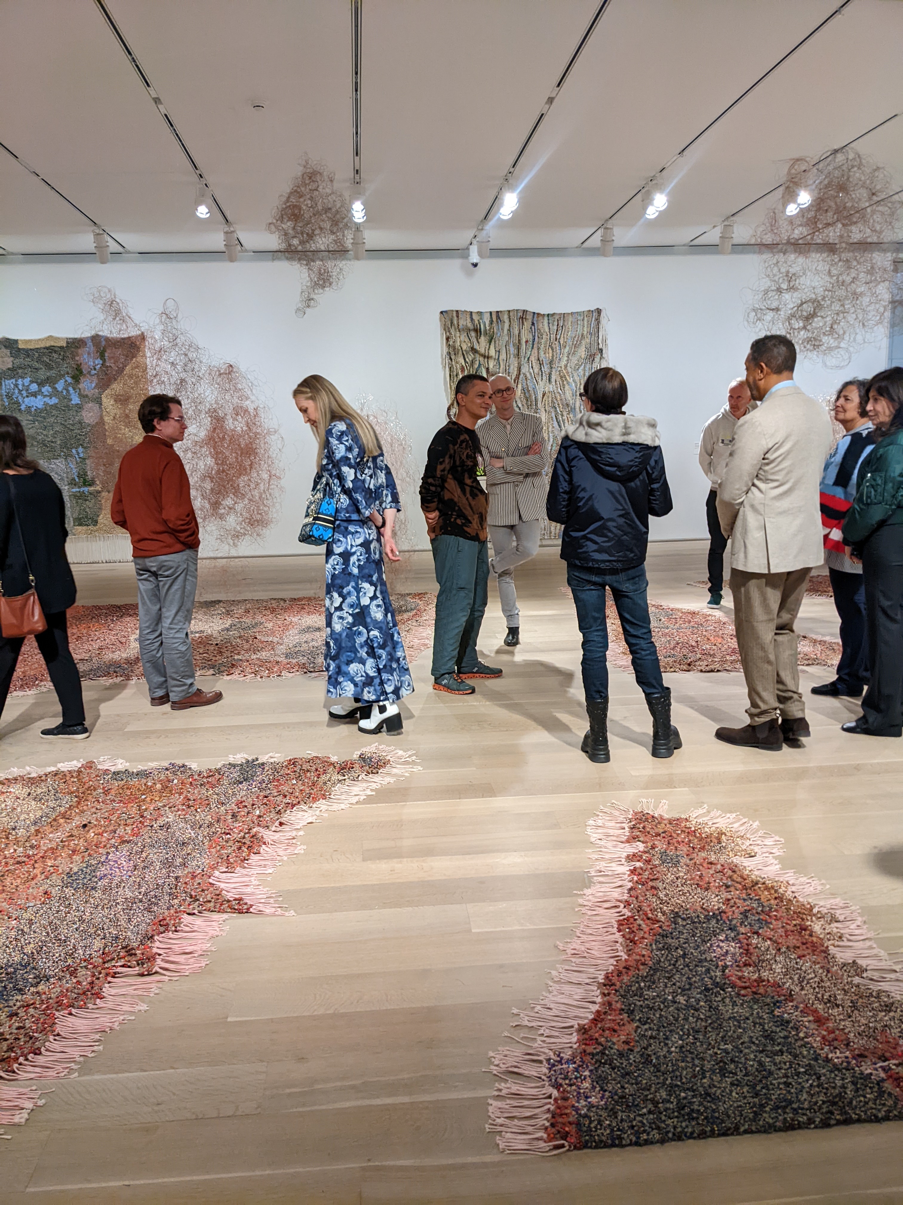 People view an exhibition of beaded works installed on the floor and walls of a gallery.